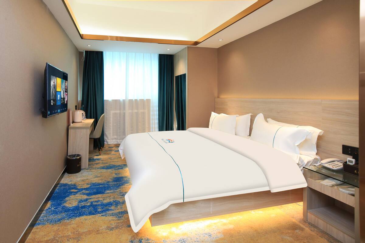 Quarto de hotel com uma cama grande, uma mesa de cabeceira com telefone e uma TV na parede.