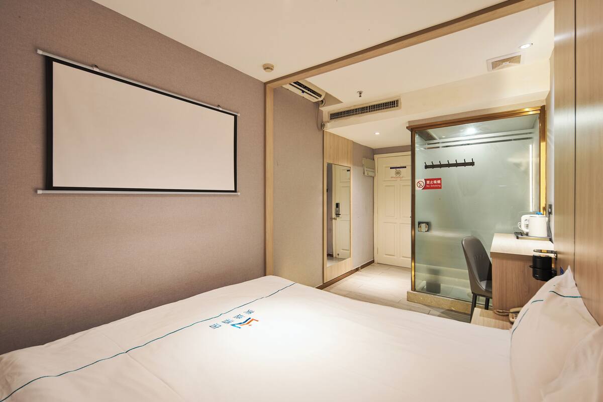 Quarto de hotel com cama, um espelho grande, secretária pequena com cafeteira e chuveiro.