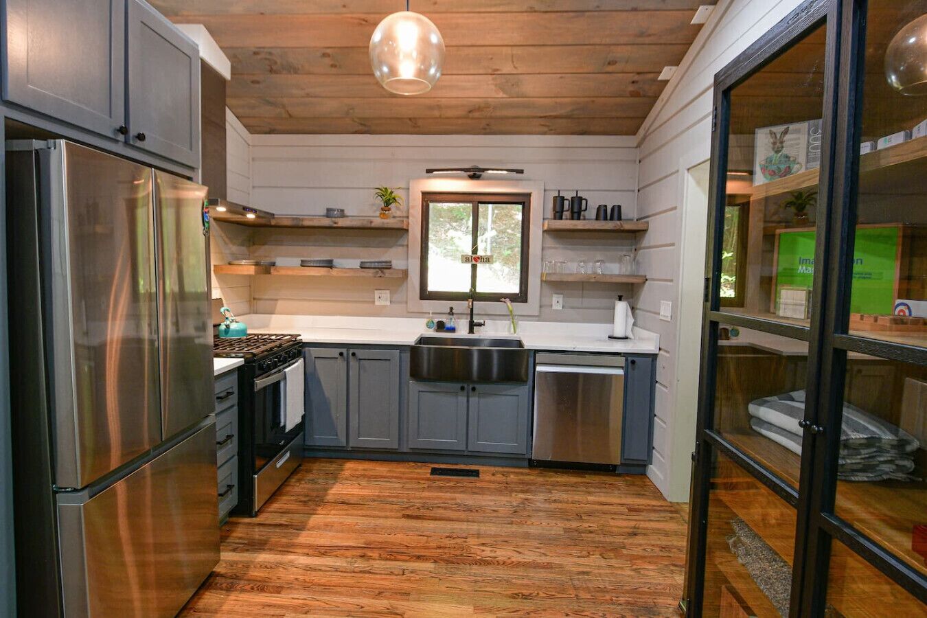 A modern kitchen with stainless steel appliances, wooden flooring, and a window providing natural light.