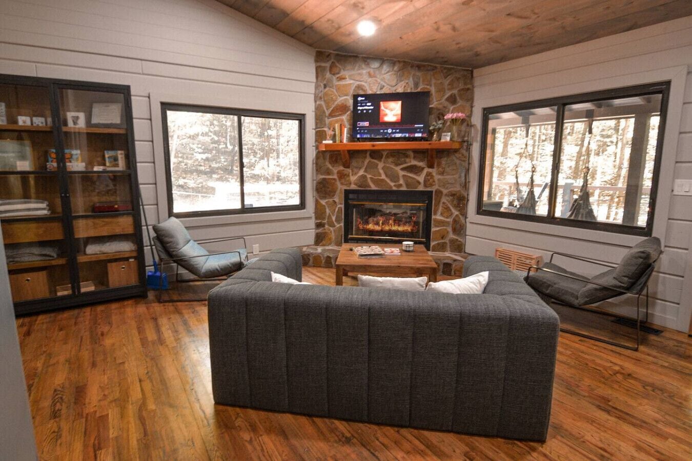 Una sala acogedora con chimenea de piedra, televisor y un amplio sofá seccional gris.