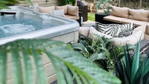 A hot tub under a wooden pergola with a hanging light, surrounded by sofas and lush greenery. - A Mythia World: Garden Oasis l Private Resort (Tobyhanna)