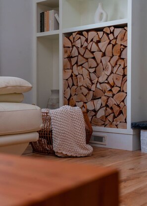 Una sala de estar con un sofá, una manta tejida, una cesta y una estantería con libros y un jarrón blanco.