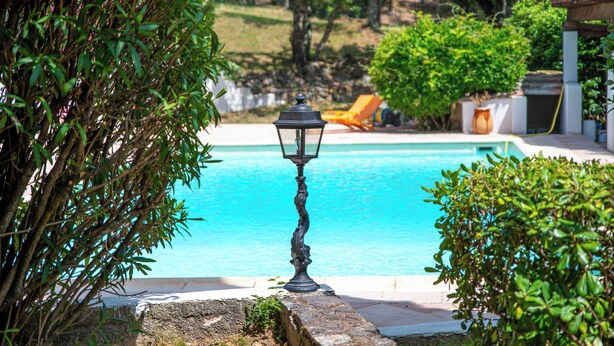 A swimming pool with a decorative lamp in the foreground, surrounded by lush greenery and a clear blue pool. - Villa Hokiss - Private pool on 1 ha of nature (Le Muy)