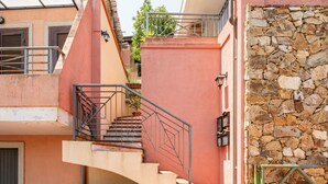 A staircase leading to a balcony with a metal railing, a stone wall, and a gate.