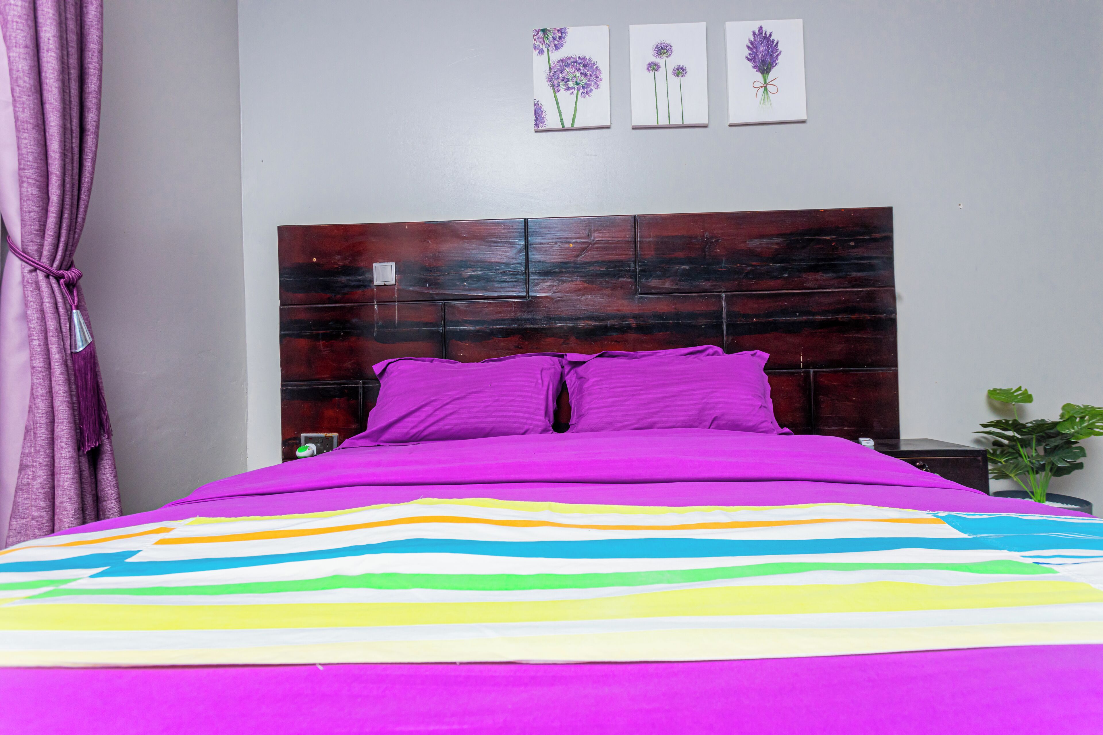 A bed with a colorful striped blanket, a wooden headboard, and purple pillows.