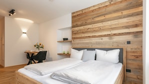 A modern bedroom with a wooden headboard, a wooden bed frame, a desk with a chair, and a small table with a vase of flowers.