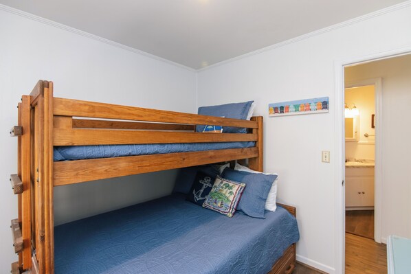 Ein Stockbett mit blauer Matratze und Kissen, ein hölzernes Kopfteil und ein an der Wand befestigtes Bücherregal.