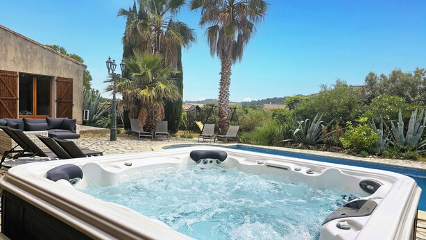 Un bain à remous avec une terrasse en pierre, des chaises longues et des palmiers.