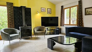 Un salon comprenant un canapé, deux fauteuils, une table basse en verre, un téléviseur et une cheminée.