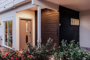 Una casa moderna con puerta de entrada de vidrio, fachada de madera oscura y una ventana pequeña.