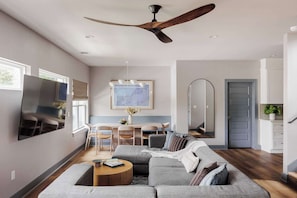 Una sala de estar moderna con ventilador de techo, televisor de pantalla plana, sofá, mesa de centro y comedor con sillas y una mesa.
