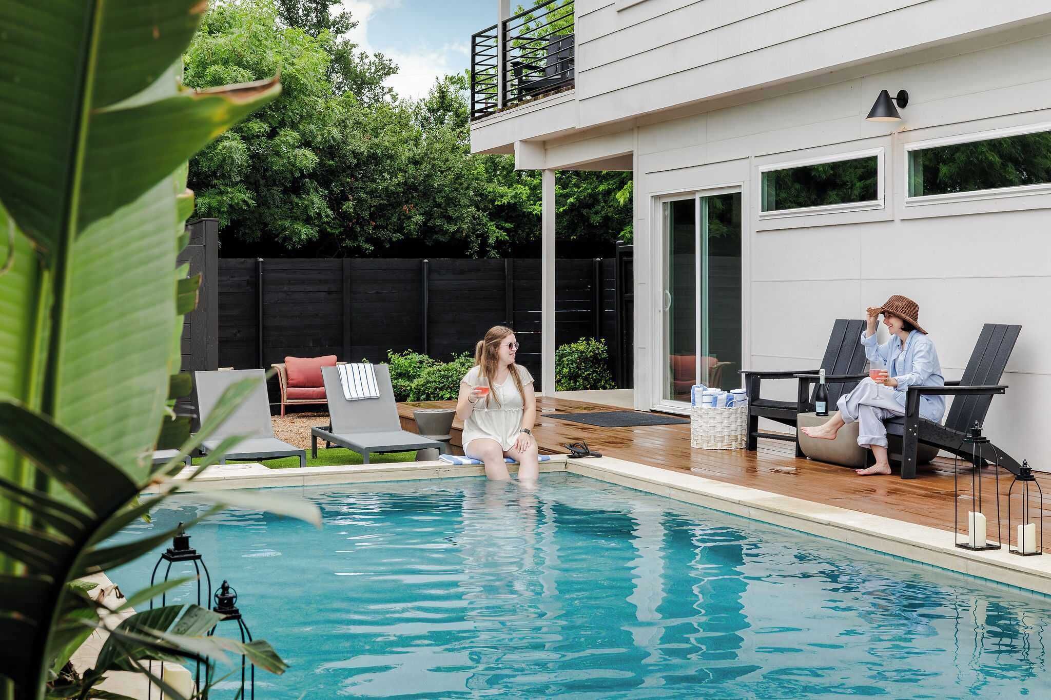 A pool area with lounge chairs, a wooden deck, and a modern building with large windows.