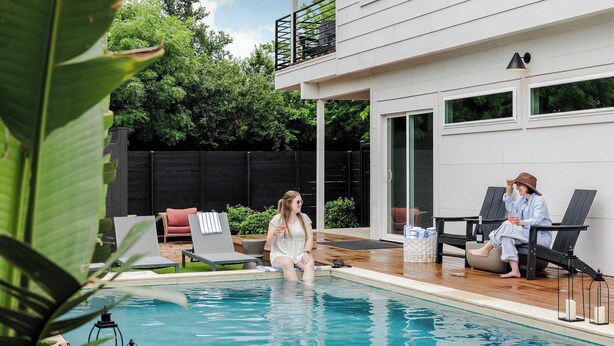 A pool area with lounge chairs, a wooden deck, and a modern building with large windows. - Rare 5BR East Austin Home | Shared Pool & DT Drive (Austin)