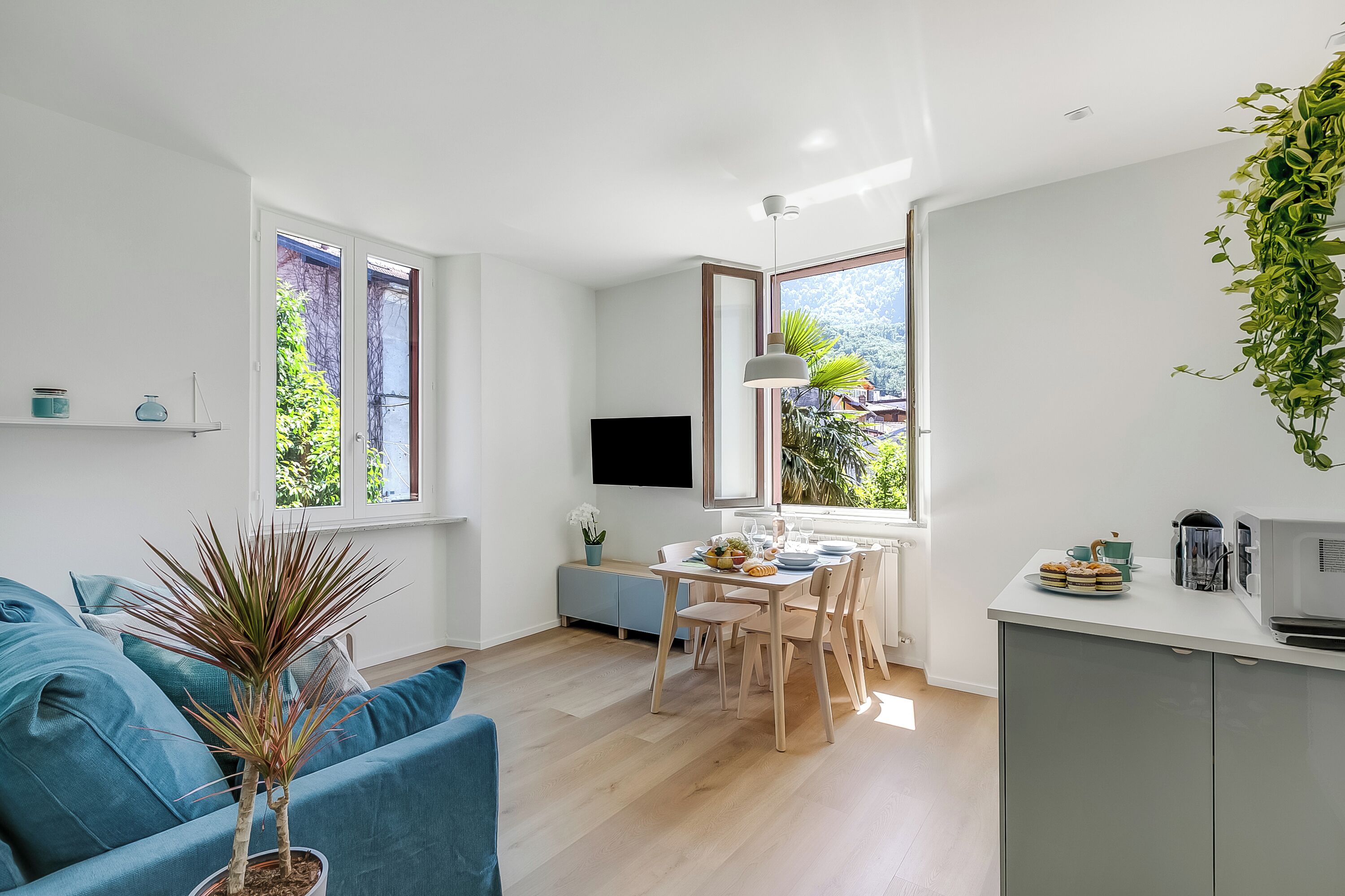 A modern living room with a blue sofa, a dining area with a table set for two, and a kitchen area with a microwave.