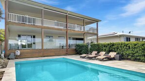 A two-story house with a swimming pool and lounge chairs.