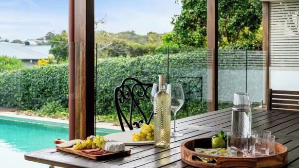 A wooden table with a bottle of white wine, a glass, and a tray with grapes and cheese.