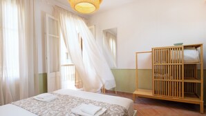 A bedroom with a bed, a wooden wardrobe, a mirror, and a window with curtains.