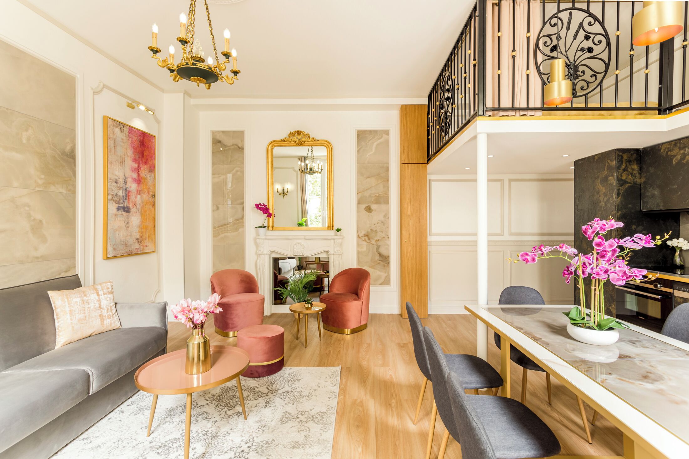 A spacious living room with a grey sofa, pink armchairs, a marble coffee table, and a dining area with a white table and chairs.
