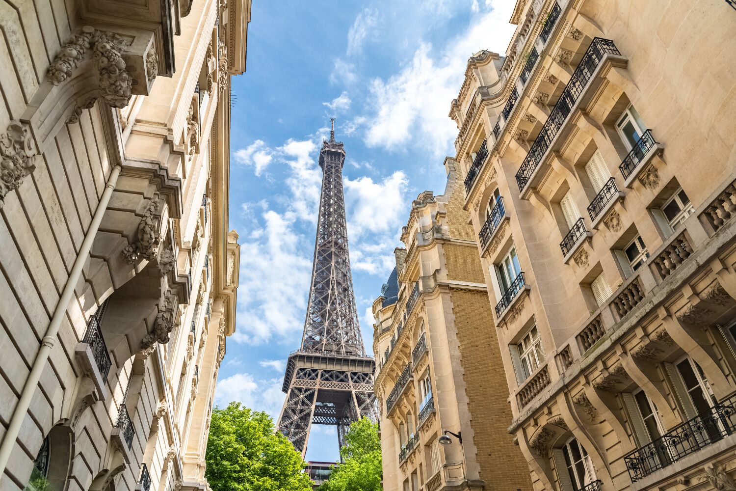 Vista de la Torre Eiffel entre dos edificios de arquitectura clásica, con balcones ornamentados y detalles en piedra.