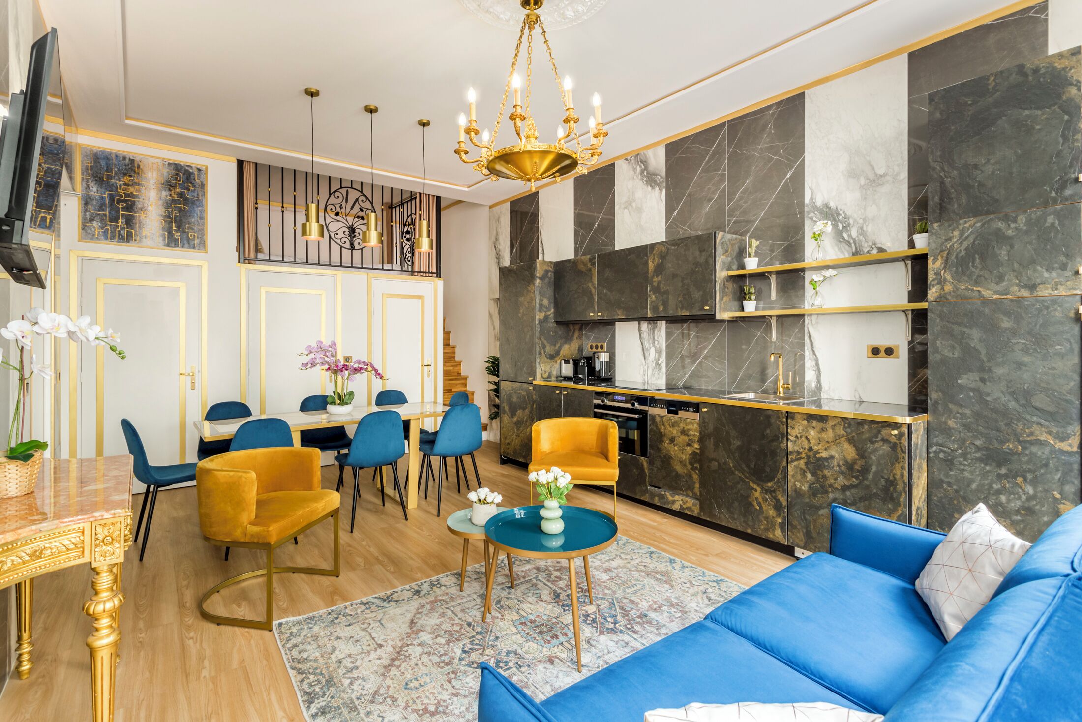 A modern living room with a blue sofa, yellow chairs, a dining table, and a kitchen area with marble countertops.