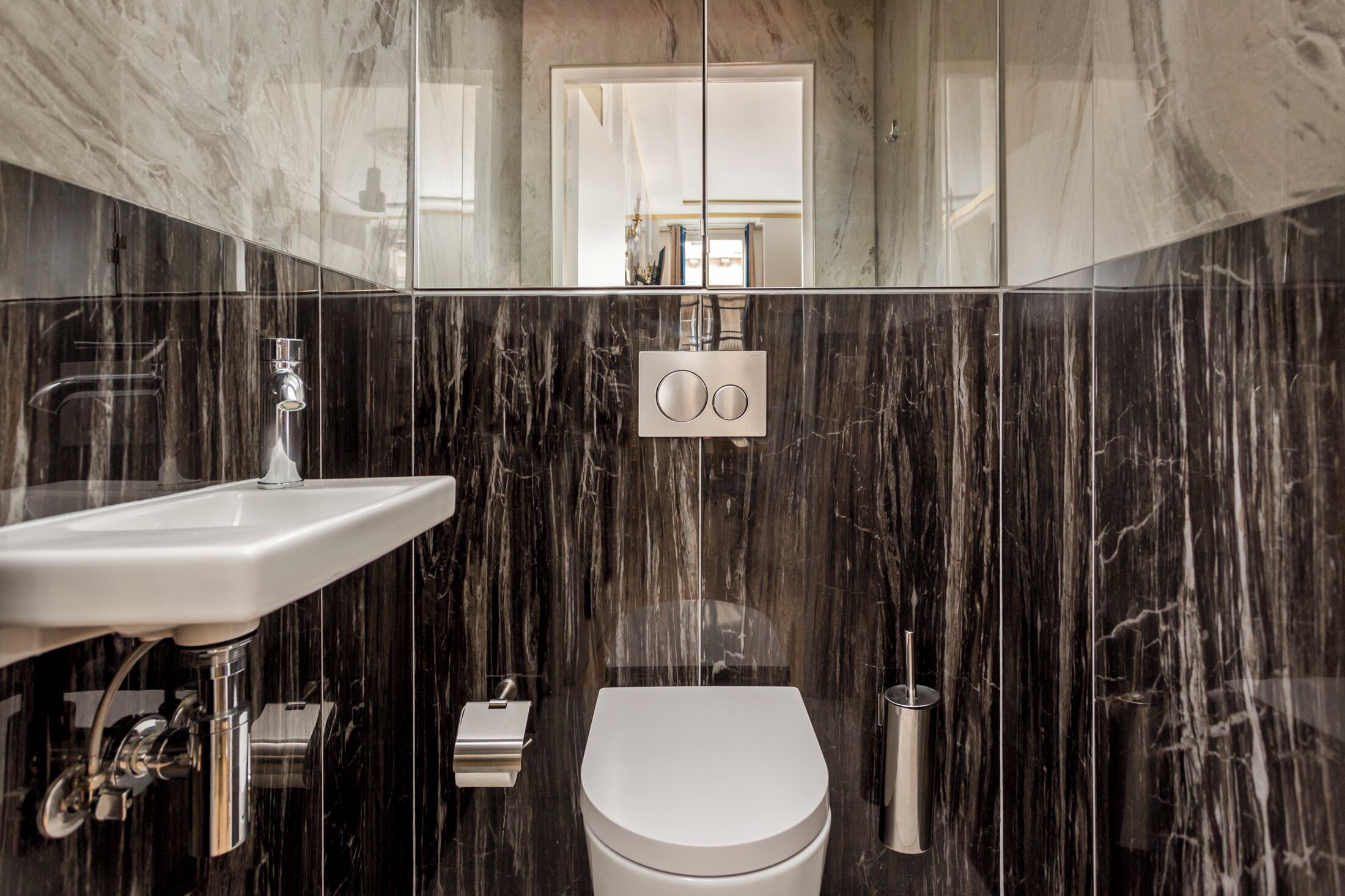 Une salle de bain moderne avec un pare-baignoire en marbre, un lavabo blanc et des toilettes.