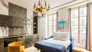Une chambre moderne avec un grand lit, un fauteuil jaune, une petite table ronde et une vue sur la ville grâce à de grandes fenêtres.