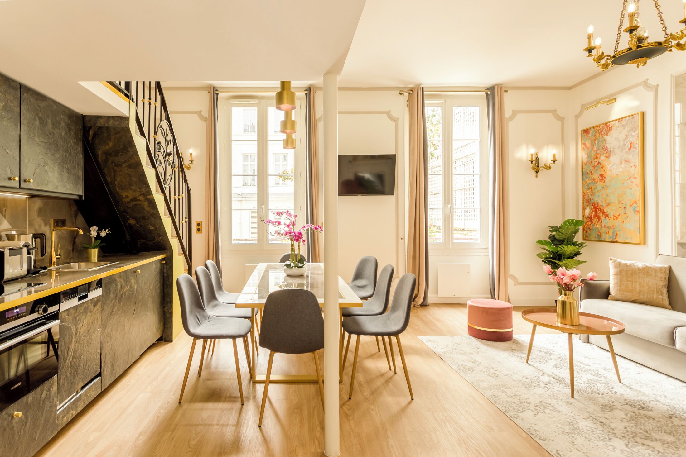 A modern living room with a dining area, a staircase, and a kitchen.