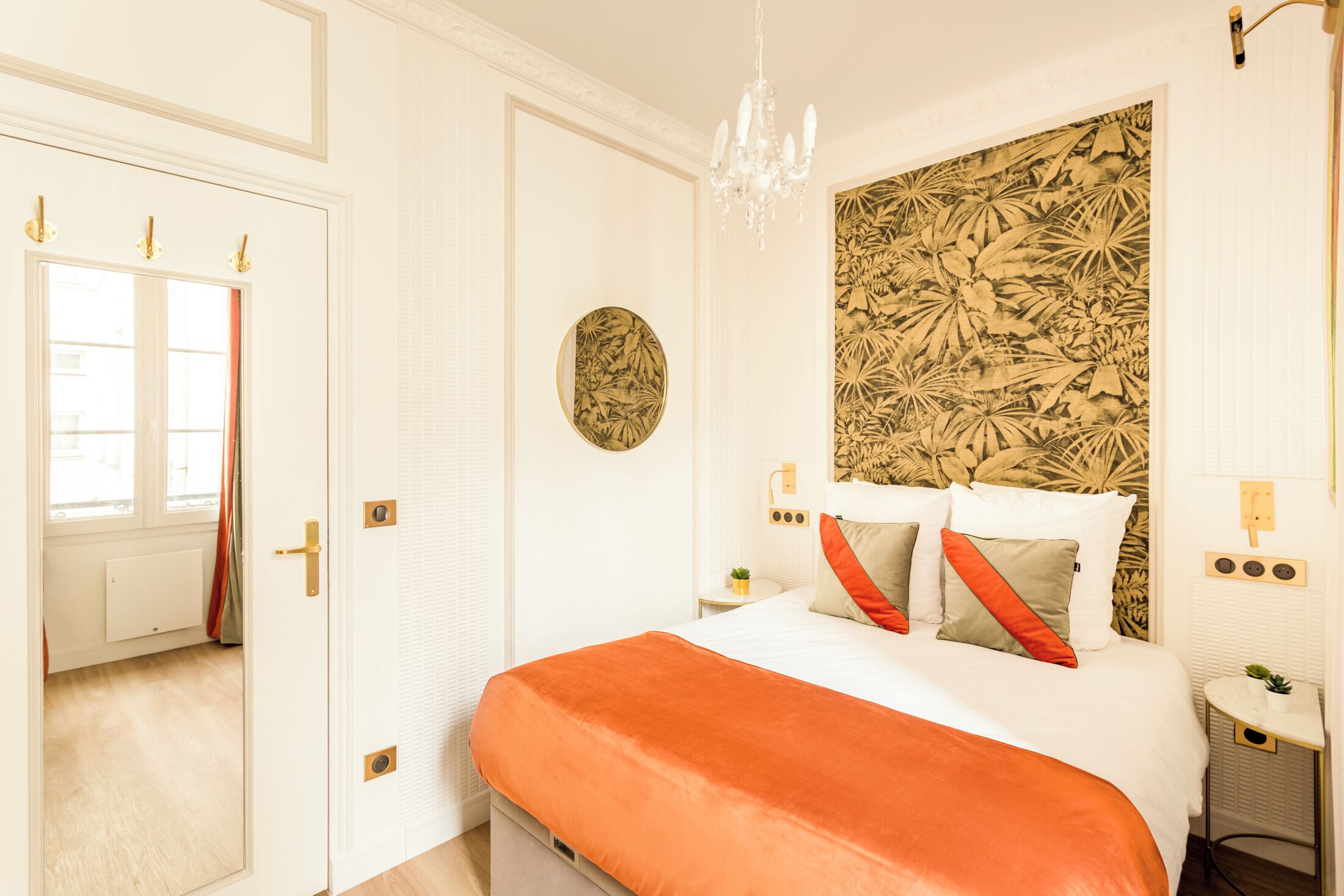 Une chambre à coucher avec un lit, un lustre, un élément décoratif rond fixé au mur et une petite table sur laquelle est posée une plante.