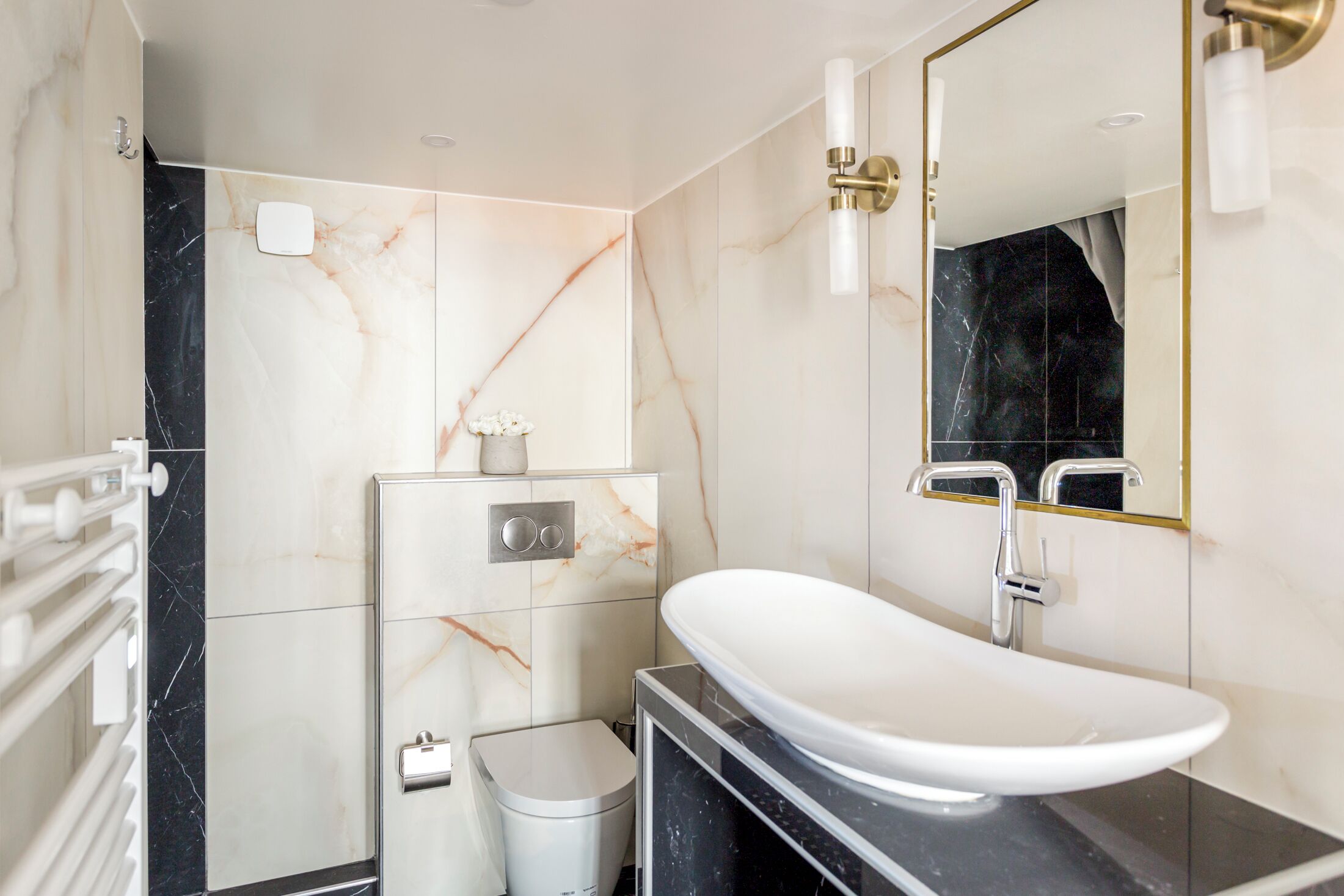 A modern bathroom with a marble vanity, a white sink, a toilet, and a large mirror.