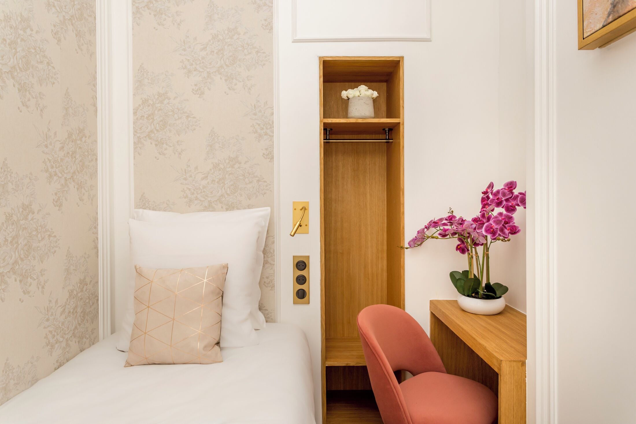 Un dormitorio con cama, un armario de madera, una silla rosa y una orquídea en maceta.
