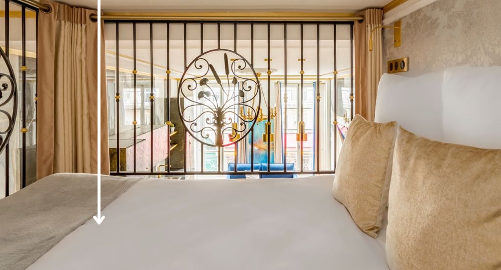A hotel room with a bed, curtains, a decorative metal gate, and a view of the outside.
