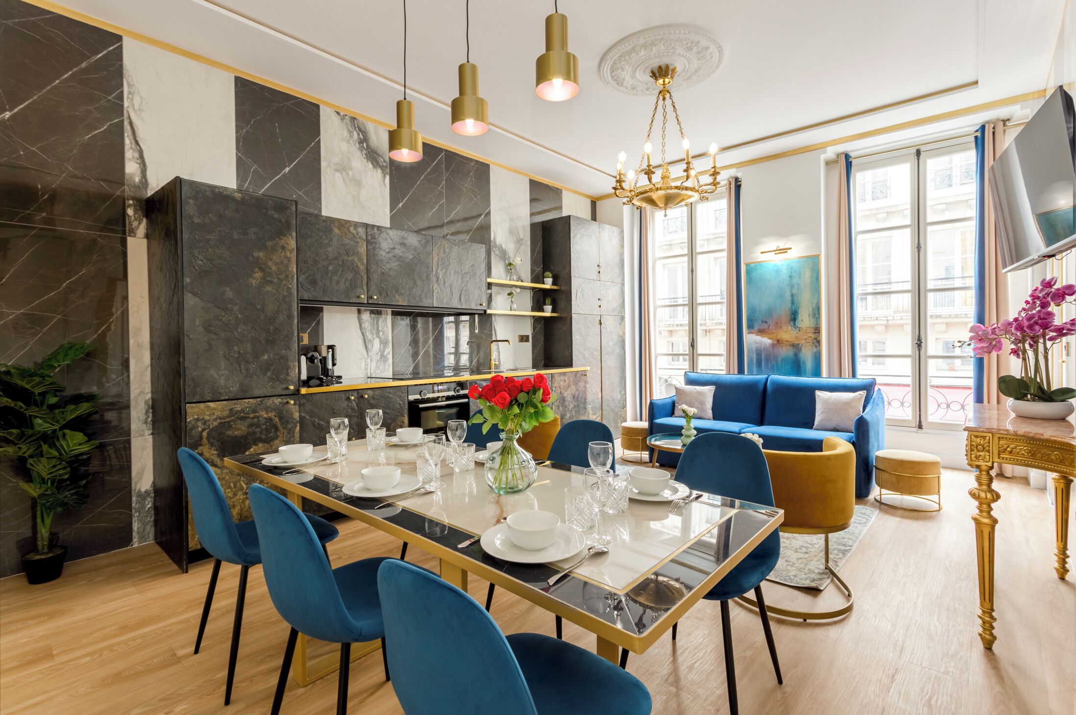A modern dining area with a marble backsplash, a chandelier, and a blue sofa in the background.