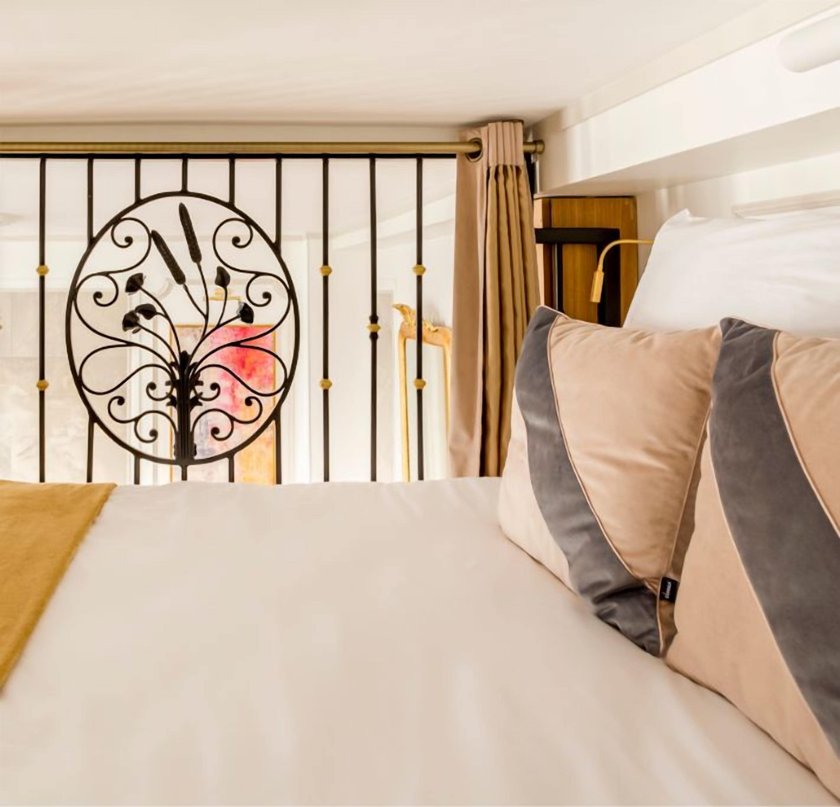 Ein Hotelzimmer mit einem Bett, beigen Vorhängen, einem dekorativen Metallgitter und einer Chandelier.