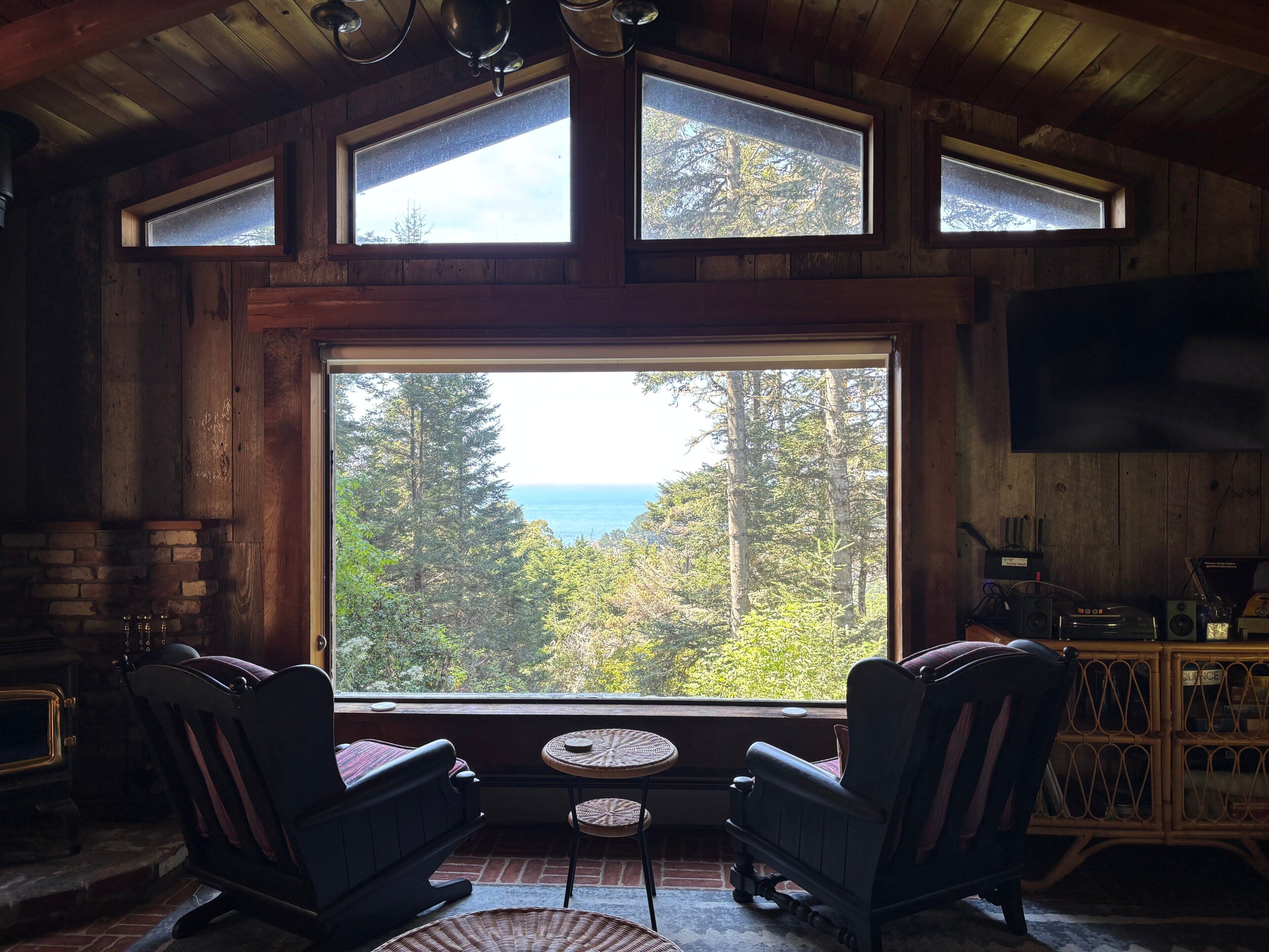 Une pièce chaleureuse avec une grande fenêtre, deux fauteuils à bascule, une petite table et une cheminée.