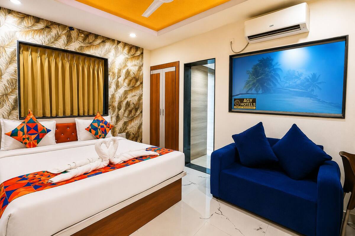 A hotel room with a bed, a blue sofa, an air conditioning unit, and a framed picture on the wall.