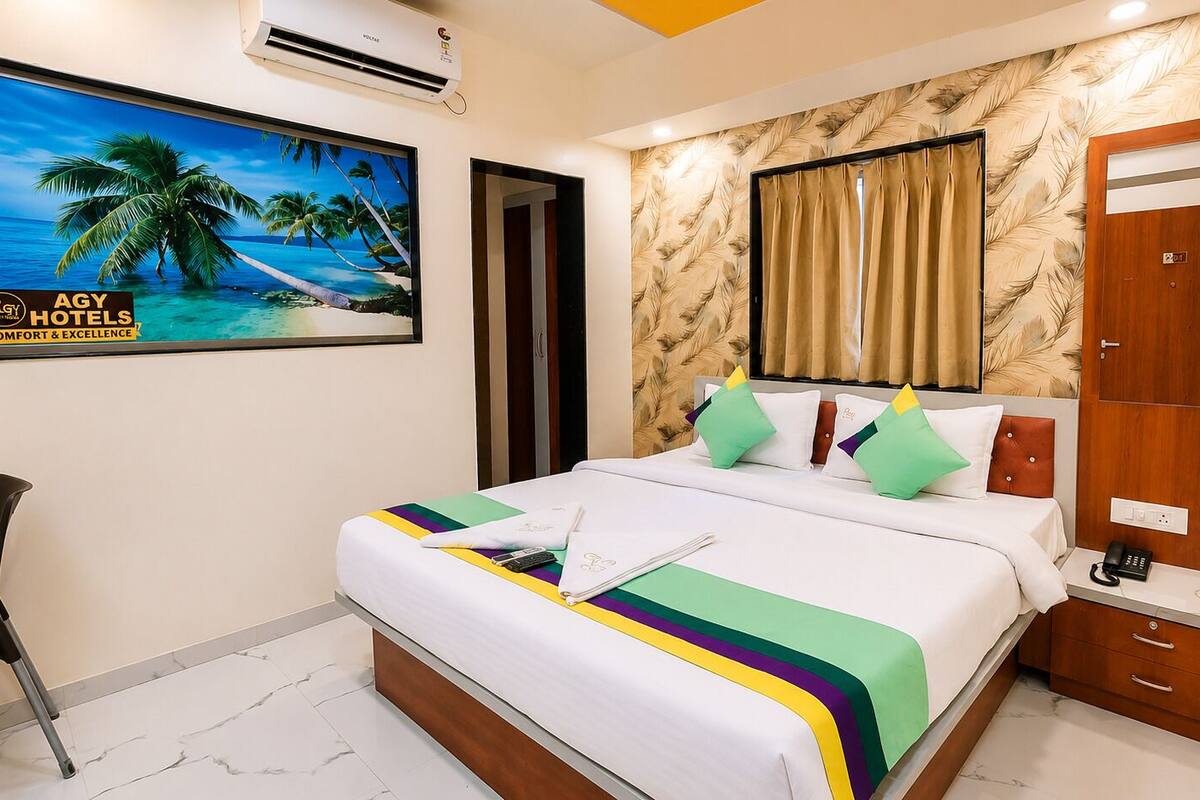 A hotel room with a bed, a desk, a chair, a painting, and a wardrobe.