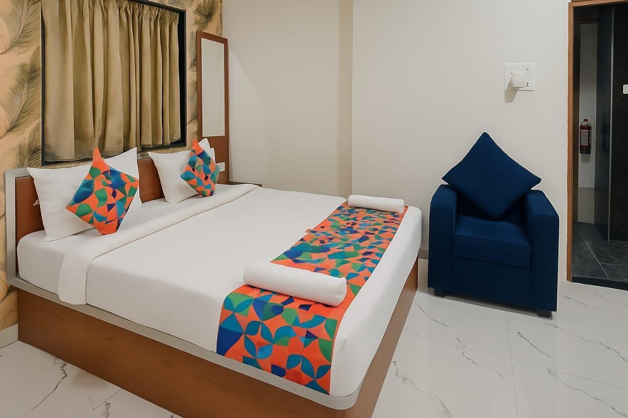 A hotel room with a bed, a blue armchair, a patterned bedspread, and a window with curtains.