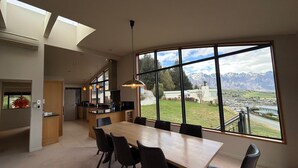 Una cocina moderna con una isla grande, un comedor con mesa y sillas de madera, y vistas a montañas a través de amplios ventanales.