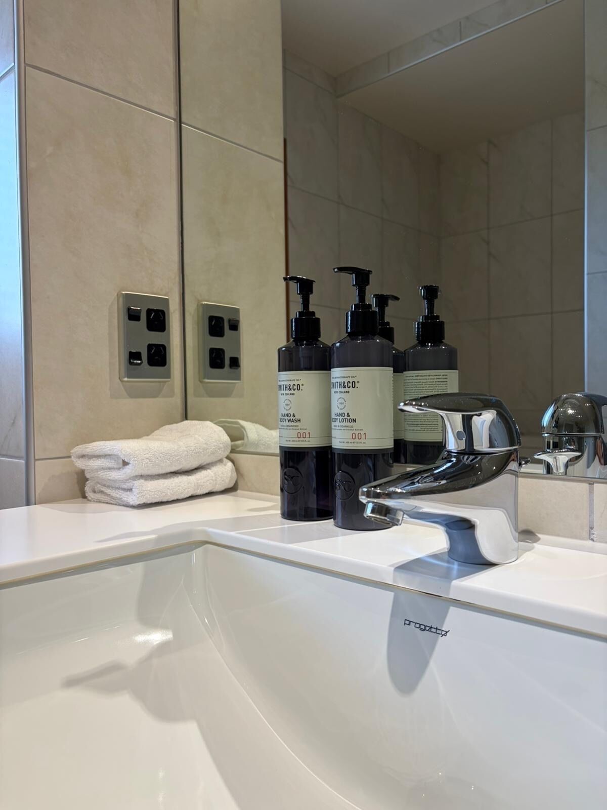 A modern bathroom with a white sink, black soap dispensers, and a mirror.