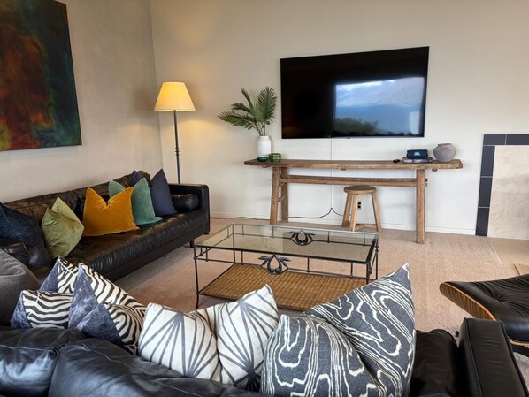 A modern living room with a leather sofa, a glass coffee table, a wooden TV stand, and a mounted TV. - Alpine Luxury on London Queenstown Hill 4B+ 3.5B (Queenstown)