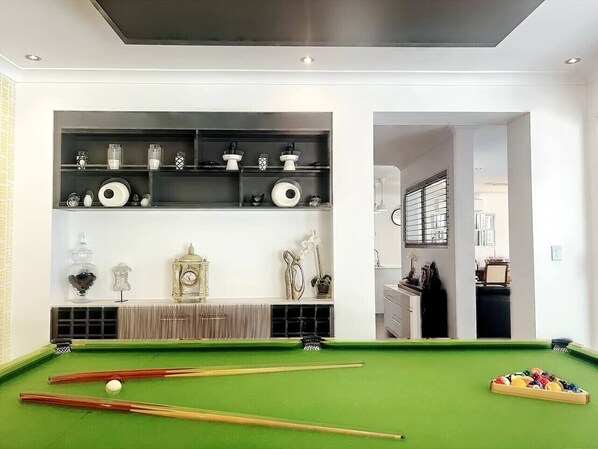 A pool table with a green felt surface, a white cue ball, and several pool cues.