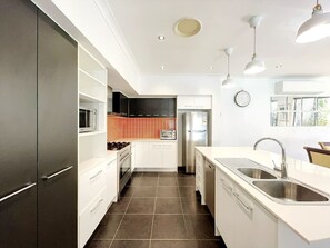 A modern kitchen with white cabinetry, a stainless steel refrigerator, a built-in oven, and a double sink.