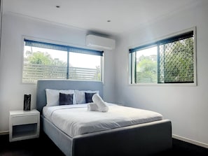 A bedroom with a bed, nightstand, and two windows with blinds.