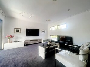A modern living room with a flat-screen TV, a sofa, a coffee table, and a white console.