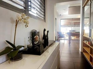 Eine moderne Hotelhalle mit Empfangstresen, einem Blumentopf, dekorativen Vasen und einem Blick auf einen Essbereich im Hintergrund.