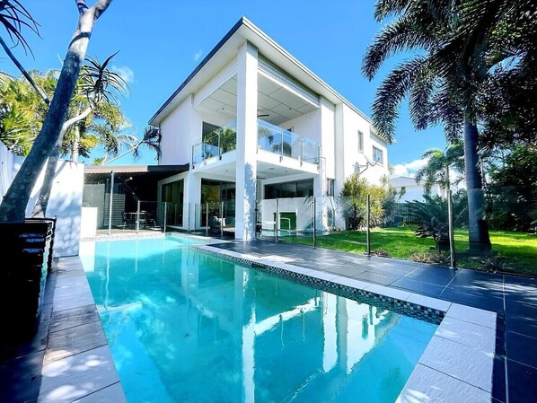 A modern house with a swimming pool, large windows, and a balcony.
