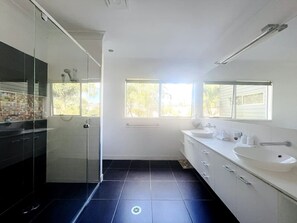 Ein modernes Badezimmer mit Duschkabine aus Glas, großem Spiegel und Fenster für natürliches Licht.