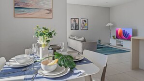 A modern living room with a dining area, a sofa, and a flat-screen TV. - 2BR Apartment w/ Balcony Near Food Shop & Transit (Macgregor)