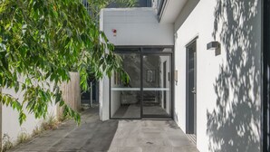 A modern building with a glass door entrance, a small outdoor seating area, and a paved pathway. - 2BR Apartment w/ Balcony Near Food Shop & Transit (Macgregor)