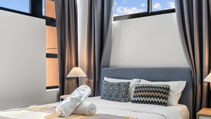 A modern hotel room with a large bed, a window with curtains, a bedside lamp, and a neatly made bed with a towel. - 2BR Apartment w/ Balcony Near Food Shop & Transit (Macgregor)